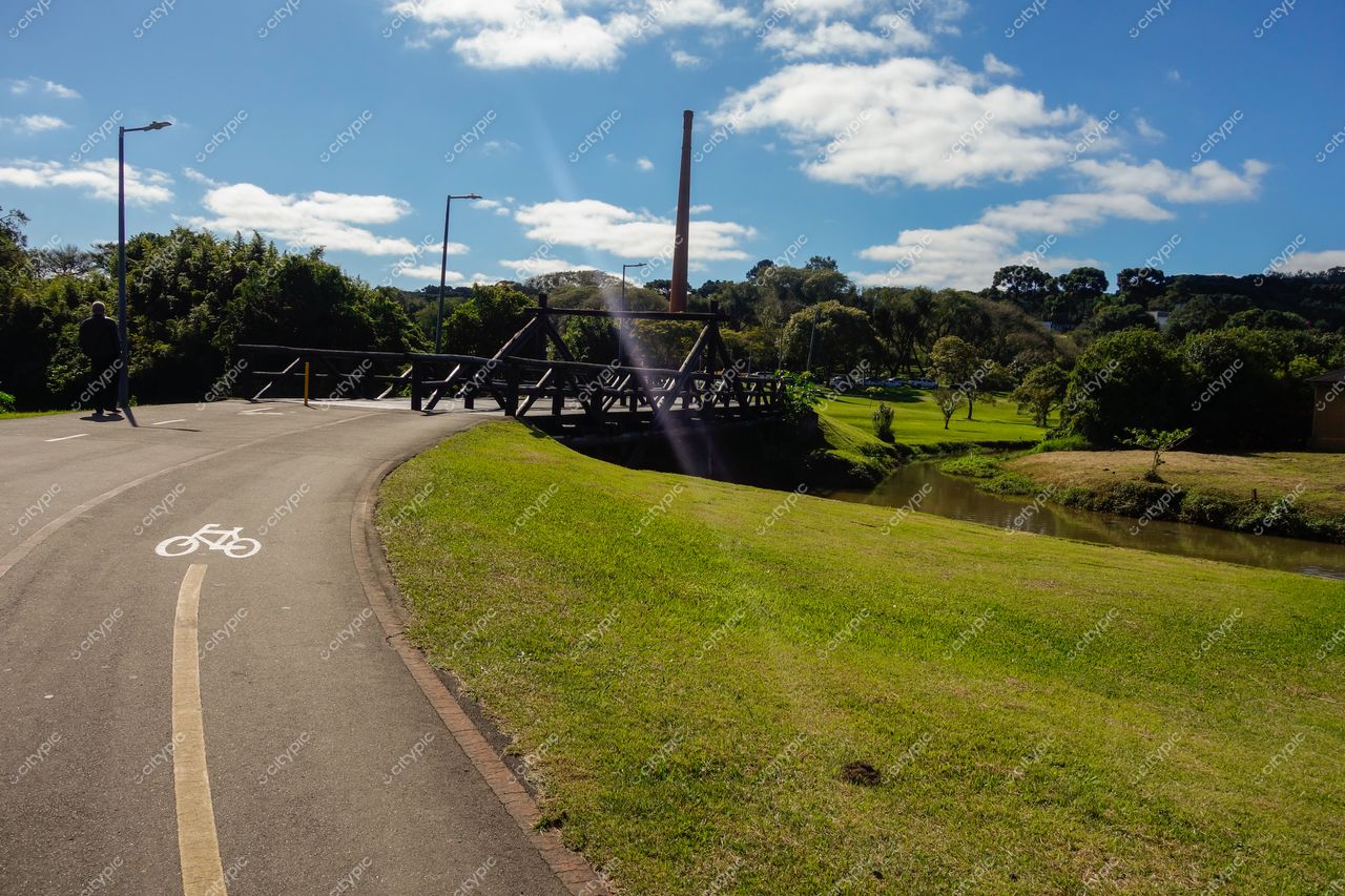 Curitiba, Paraná caminho pavimentado para ciclistas ao lado de área verde com ponte de madeira e vegetação densa