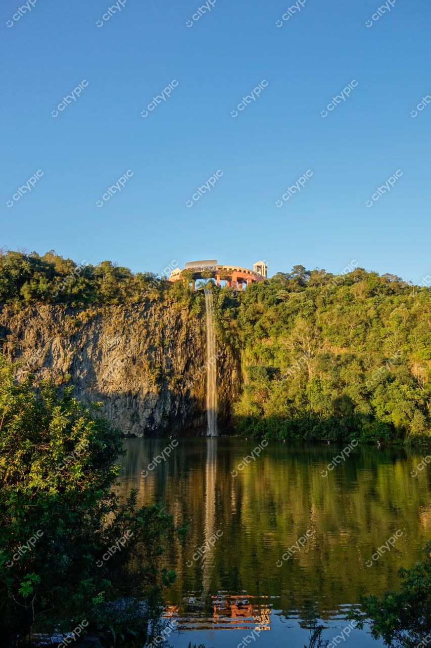 Curitiba, Paraná vista da cascata em penhasco verdejante com lago tranquilo e arquitetura colorida ao fundo