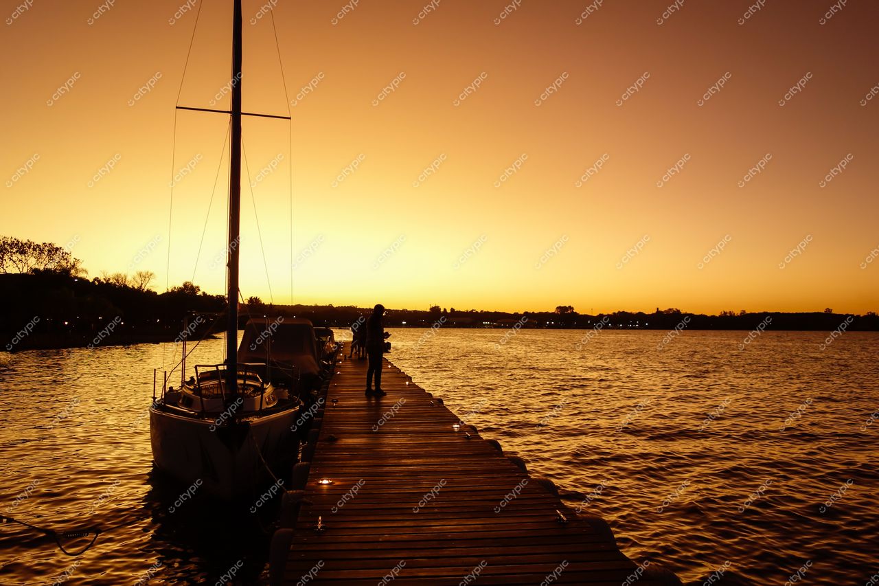 Brasília, Distrito Federal, fim de tarde com píer de madeira, barco a vela e silhueta humana ao pôr do sol
