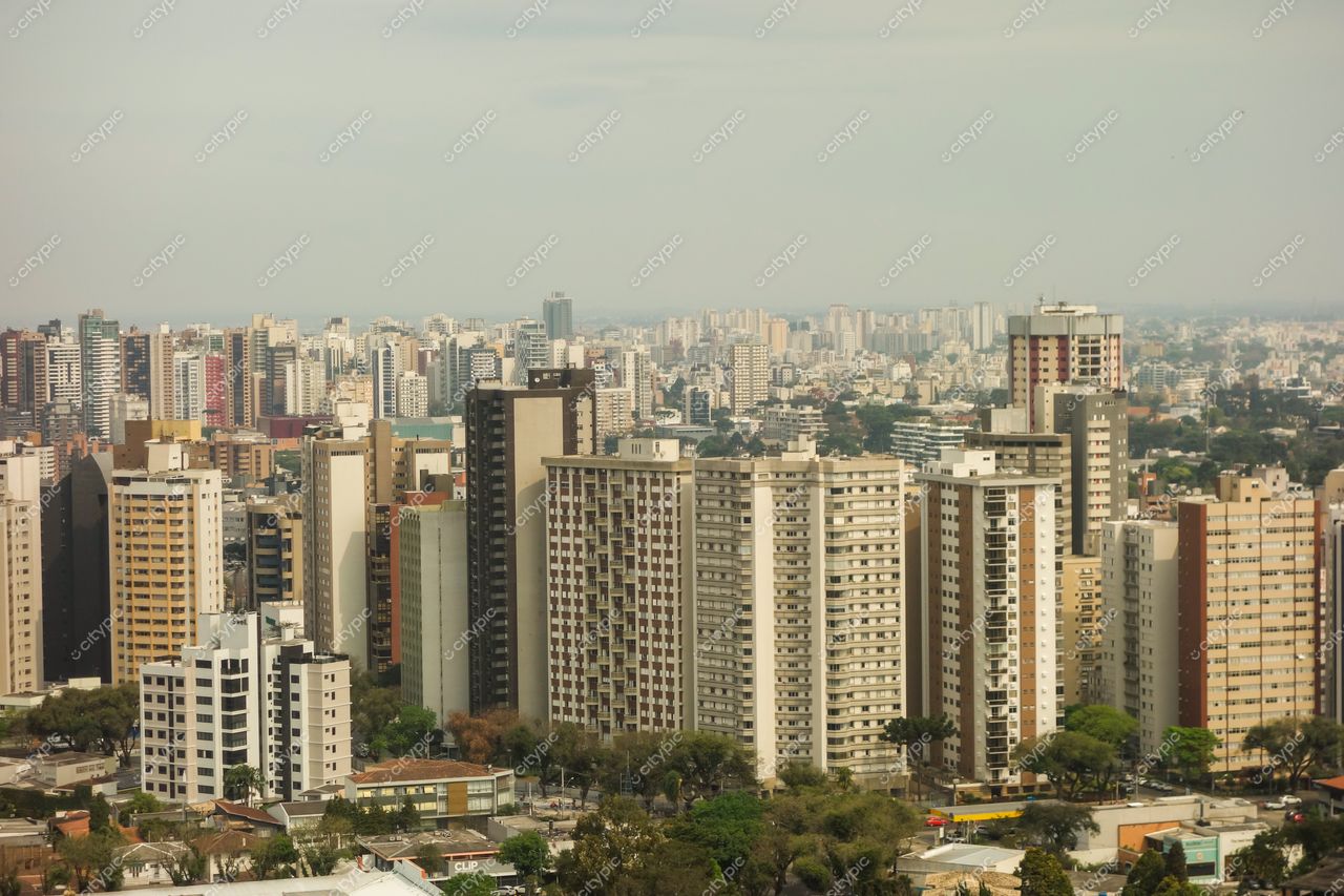Curitiba, Paraná vista panorâmica de edifícios variados em dia nublado com árvores entre os prédios e horizonte extenso