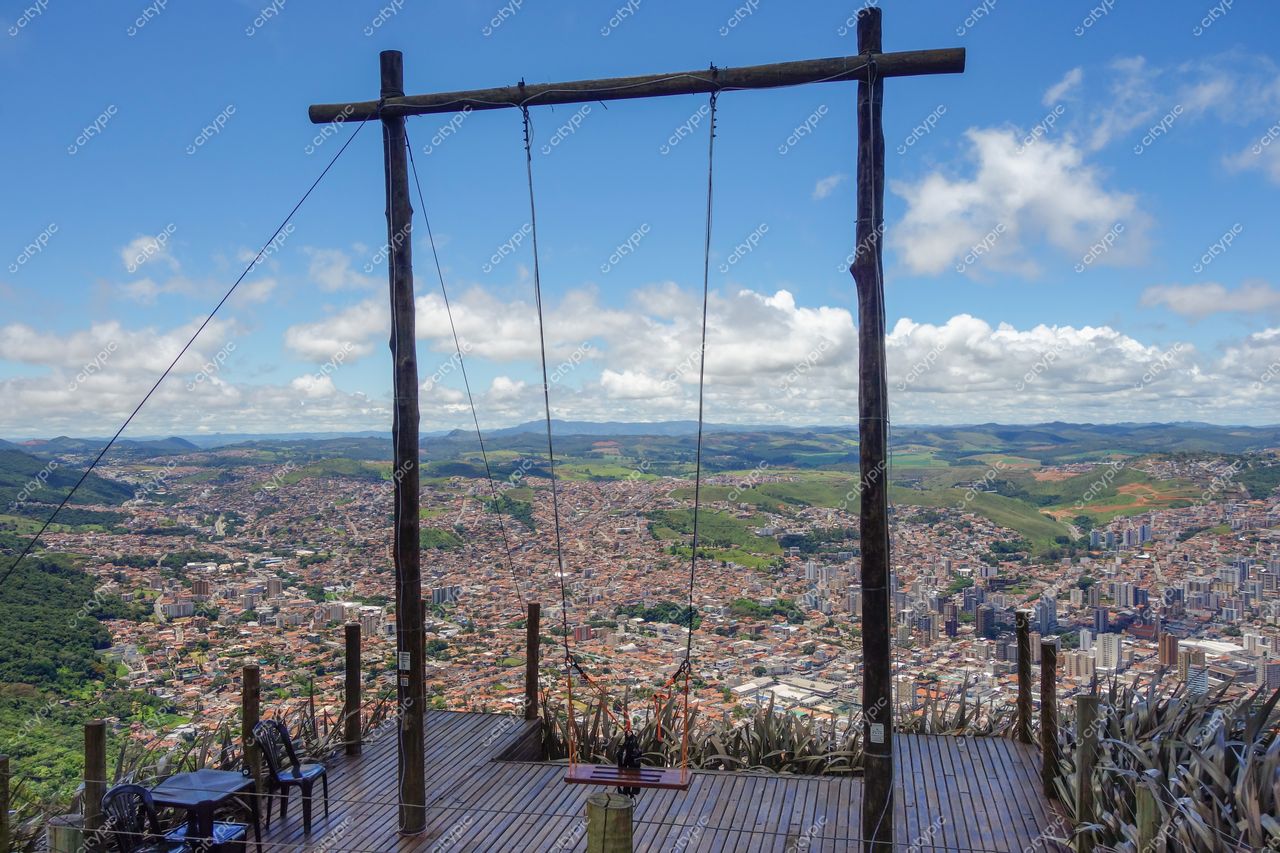 Poços de Caldas, Minas Gerais com balanço suspenso em mirante e deck de madeira sob céu azul e colinas verdes