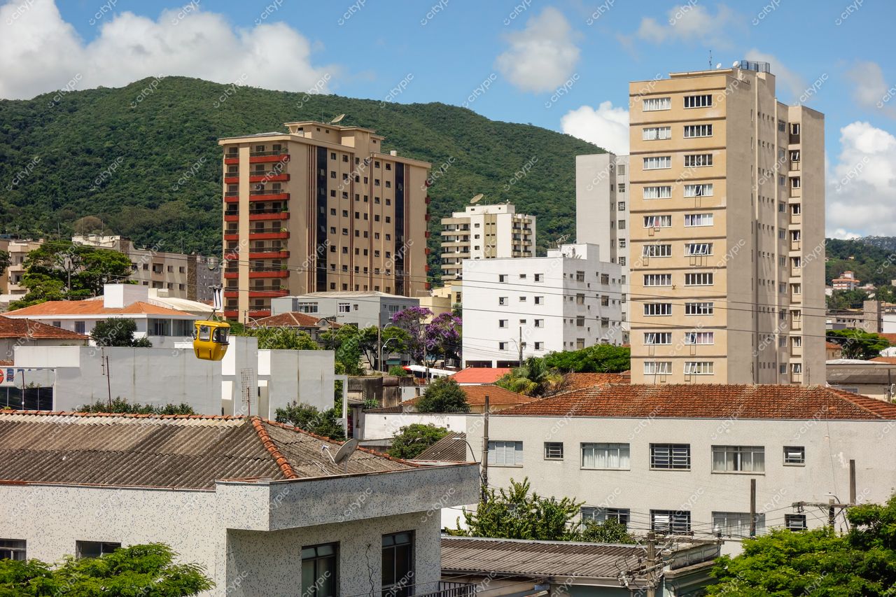 Poços de Caldas, Minas Gerais com vista urbana de prédios modernos e tradicionais sob céu parcialmente nublado e montanhas verdes