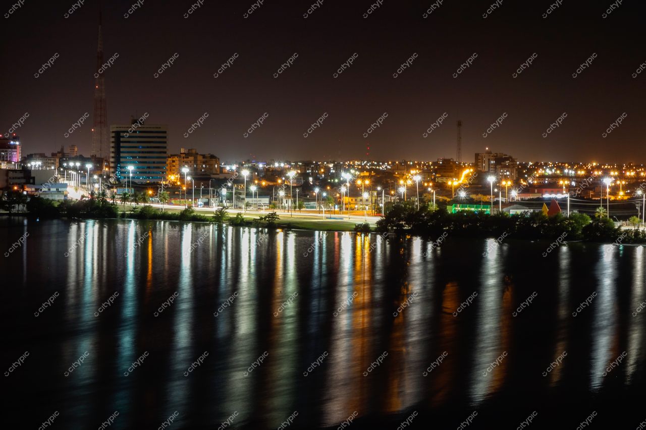 São Luís, Maranhão à noite com edifícios iluminados refletindo na água e áreas verdes nas margens urbanas