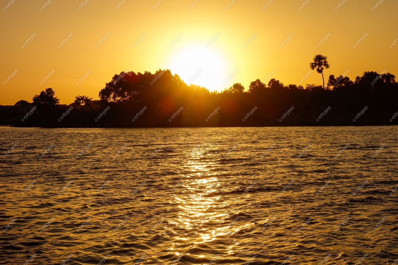Barreirinhas, Maranhão, pôr do sol refletindo luz dourada nas águas calmas de um rio com vegetação exuberante