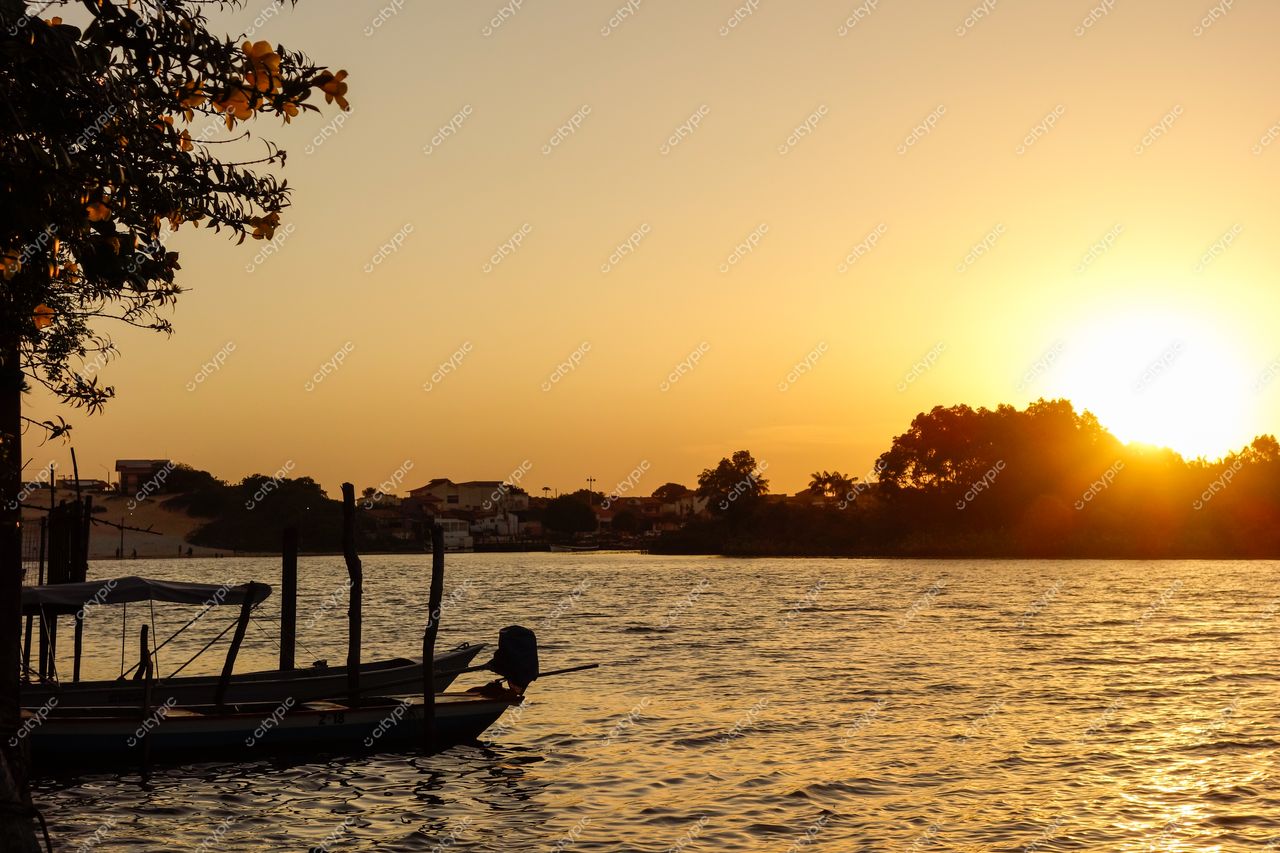 Barreirinhas, Maranhão, pôr do sol sobre rio tranquilo com embarcação de madeira e vegetação rasteira à margem