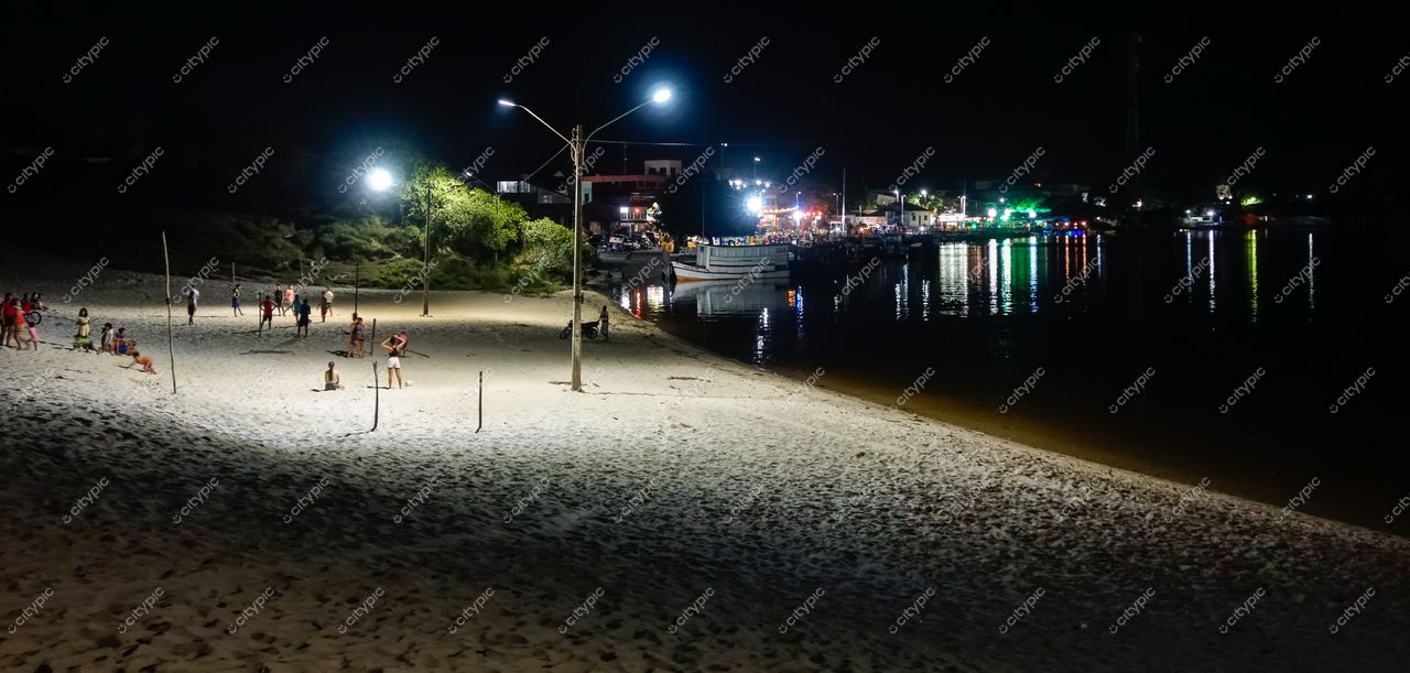 Barreirinhas, Maranhão, praia iluminada à noite com pessoas na areia e barco ancorado ao fundo