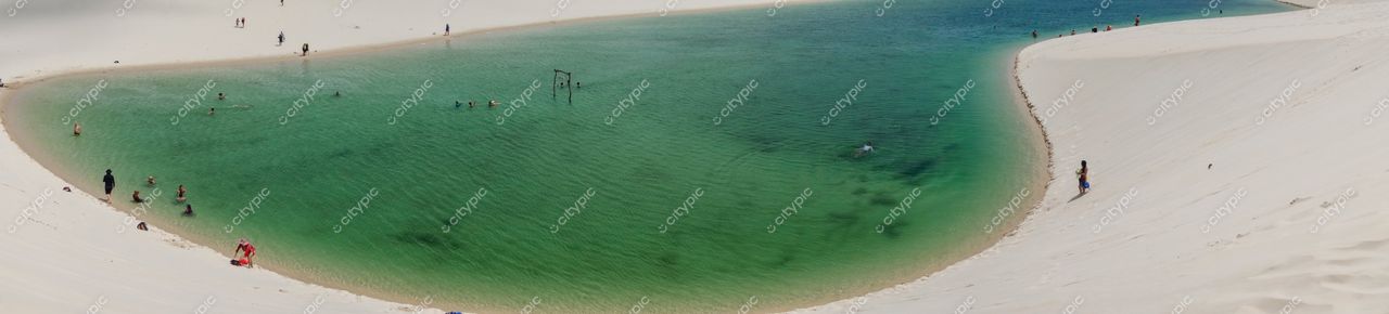 Lençóis Maranhenses, Maranhão, lagoa verde entre dunas brancas com pessoas se refrescando sob luz natural do dia