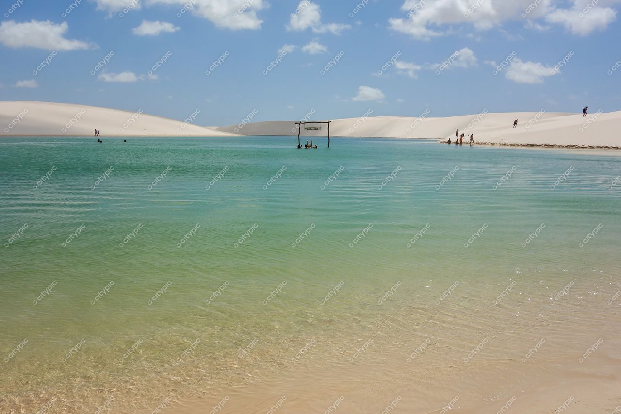 Lençóis Maranhenses, Maranhão, lagoas cristalinas em tons de verde e azul sob céu parcialmente nublado com pessoas na margem