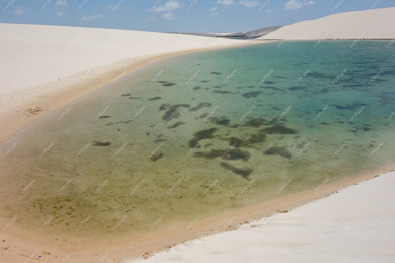 Lençóis Maranhenses, Maranhão, lagoa de águas cristalinas cercada por dunas brancas sob céu azul claro e nuvens