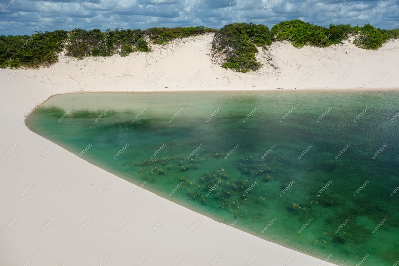 Lençóis Maranhenses, Maranhão, lagoa azul e verde entre dunas brancas com vegetação rasteira sob céu nublado