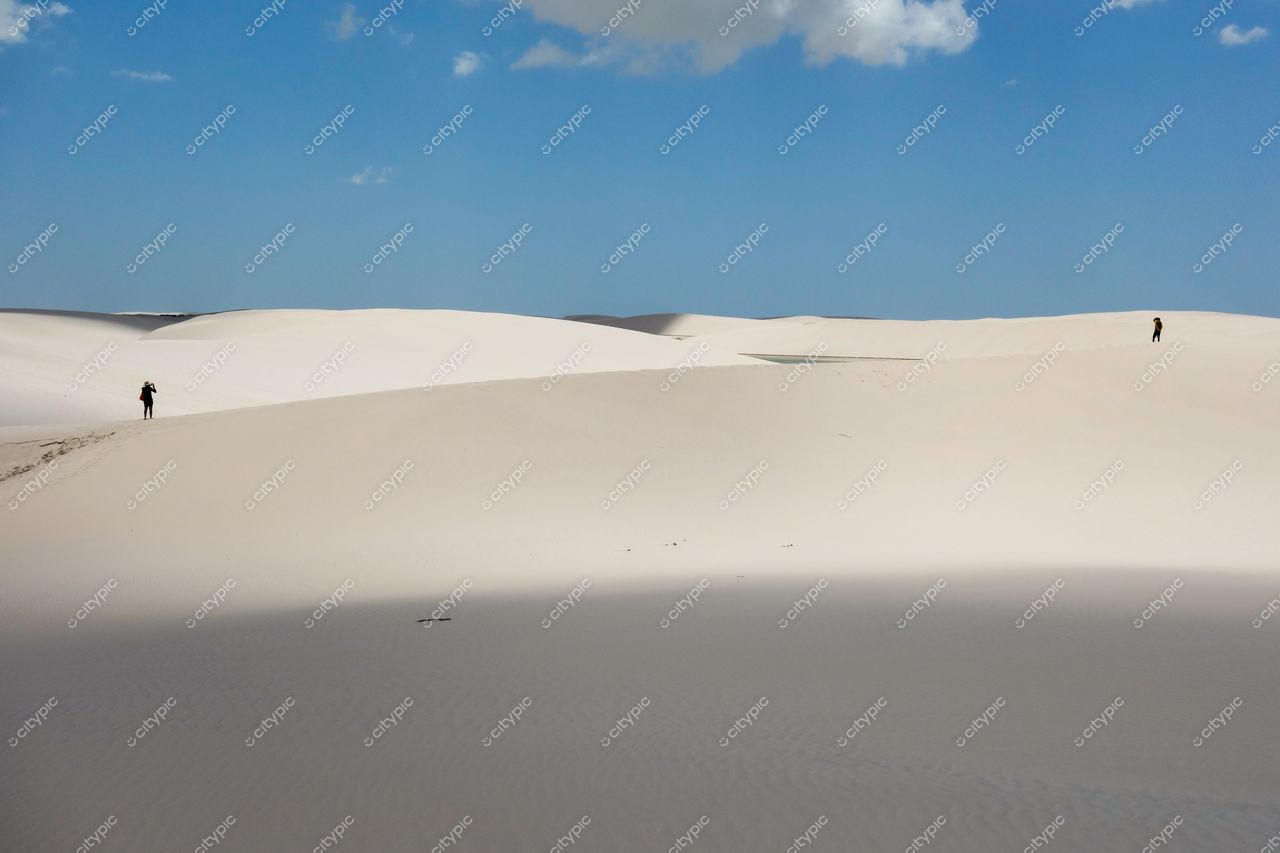Lençóis Maranhenses, Maranhão com dunas brancas sob céu azul e nuvens, figuras humanas caminhando à distância