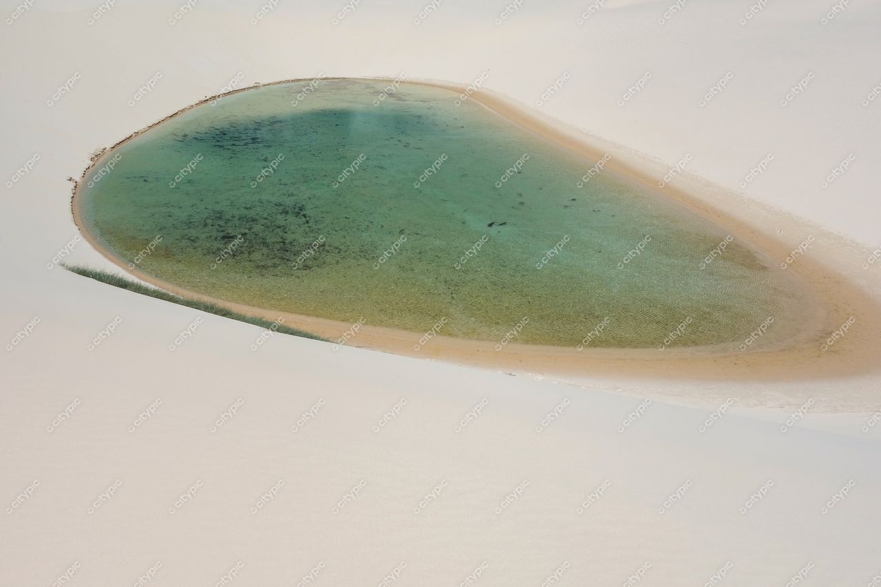 Lençóis Maranhenses, Maranhão, lagoa oval cercada por dunas brancas e vegetação nas bordas em dia ensolarado
