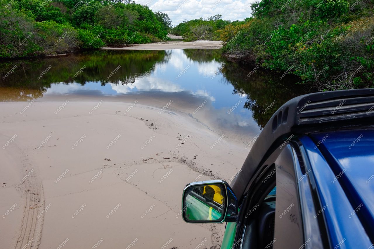 Lençóis Maranhenses, Maranhão, veículo 4×4 estacionado à beira de lagoa tranquila com vegetação densa e céu ensolarado
