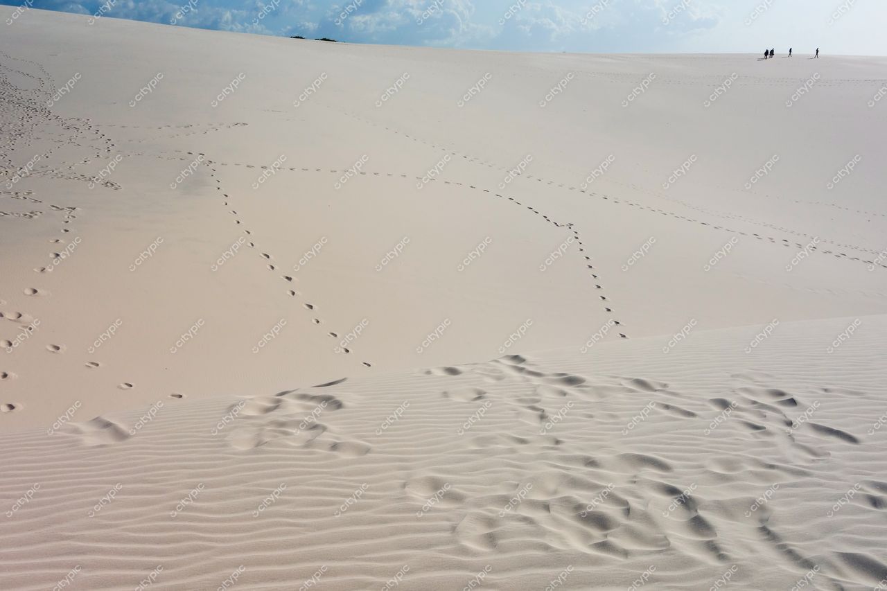 Lençóis Maranhenses, Maranhão, vastas dunas de areia clara com céu nublado e pessoas no topo da duna ao fundo