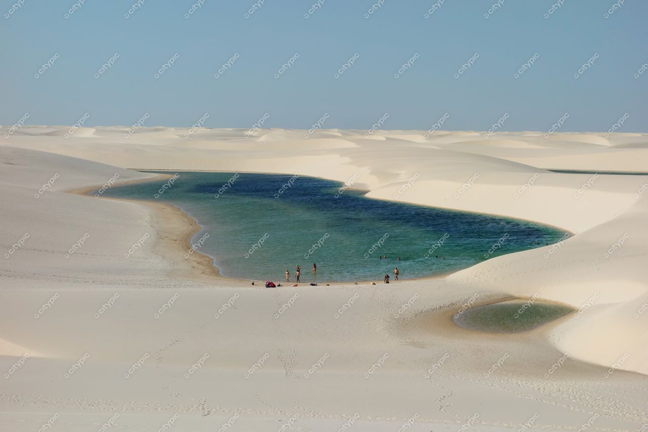 Lençóis Maranhenses, Maranhão, lagoa de águas cristalinas cercada por dunas brancas em dia ensolarado com pessoas na margem