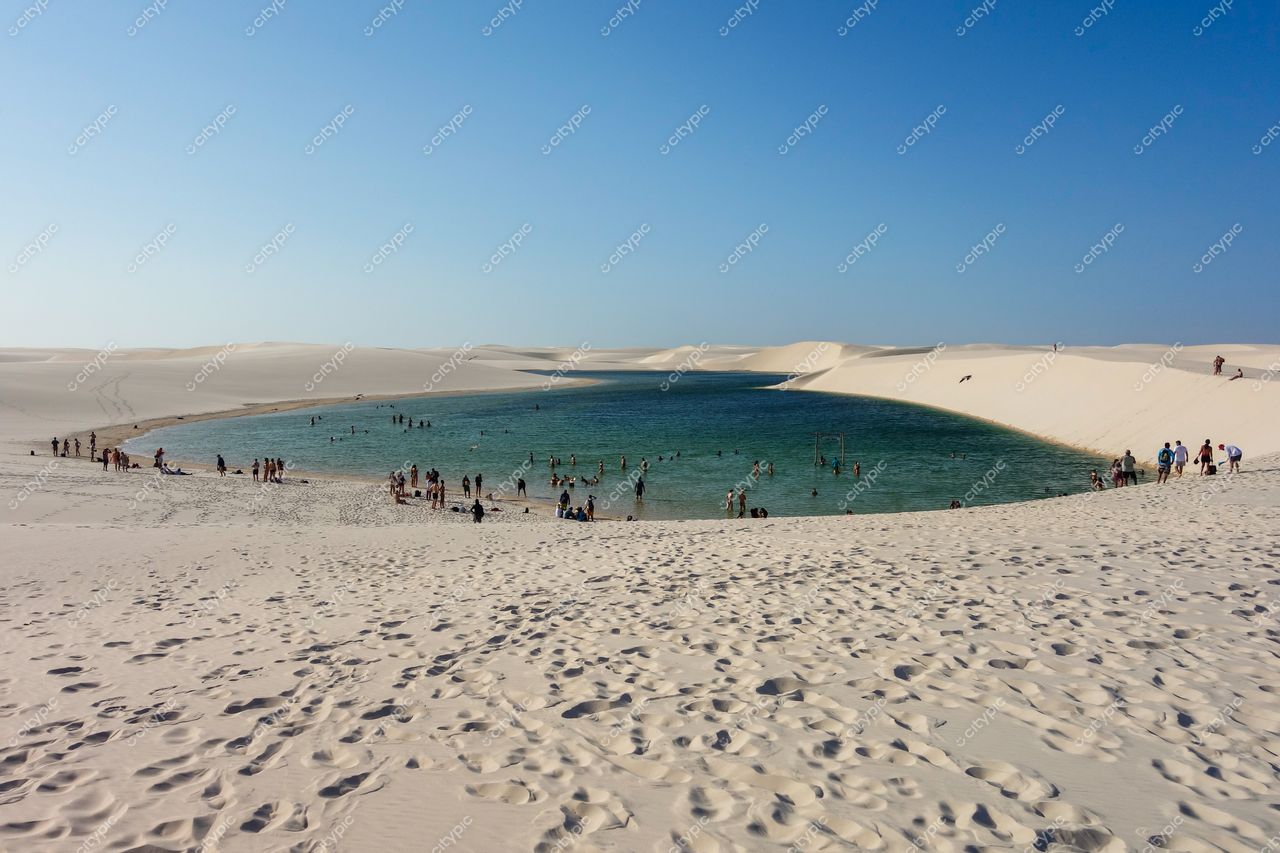 Lençóis Maranhenses, Maranhão, dia ensolarado com pessoas relaxando na areia e lago de águas cristalinas entre dunas brancas