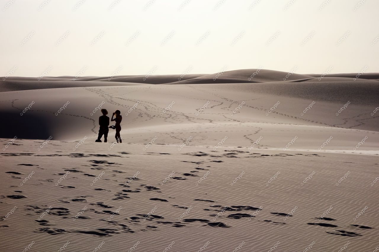 Lençóis Maranhenses, Maranhão, dois indivíduos caminhando nas dunas sob luz suave do amanhecer em paisagem tranquila