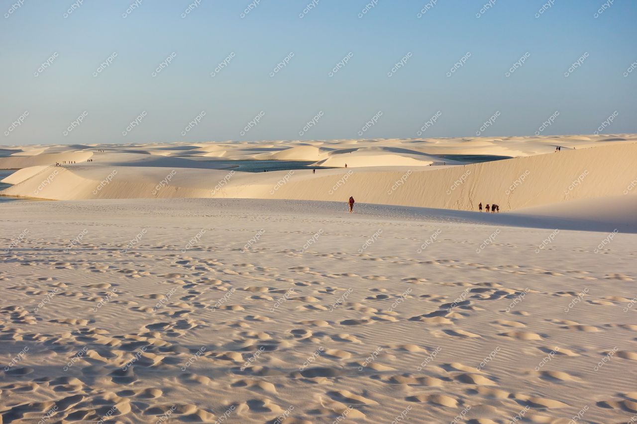 Lençóis Maranhenses, Maranhão, dunas brancas sob céu azul com pessoas ao entardecer em iluminação suave