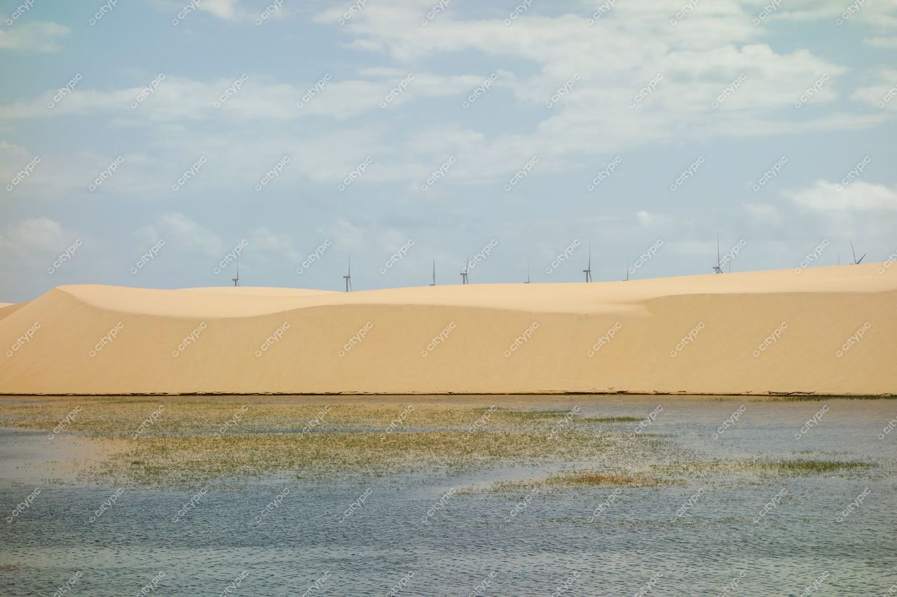 Atins, Maranhão com dunas de areia clara e turbinas eólicas ao fundo em dia ensolarado e céu azul claro