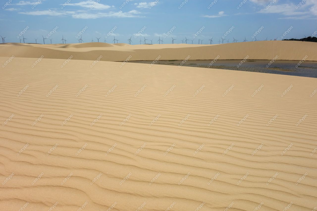 Atins, Maranhão vista das dunas amareladas com lago refletindo o céu e turbinas eólicas ao fundo