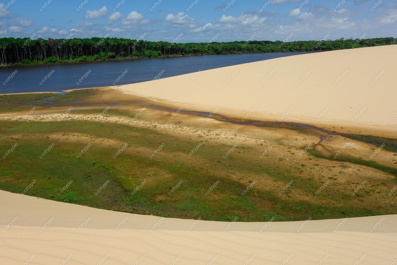 Atins, Maranhão vista das dunas de areia clara com rio calmo e vegetação exuberante sob céu nublado