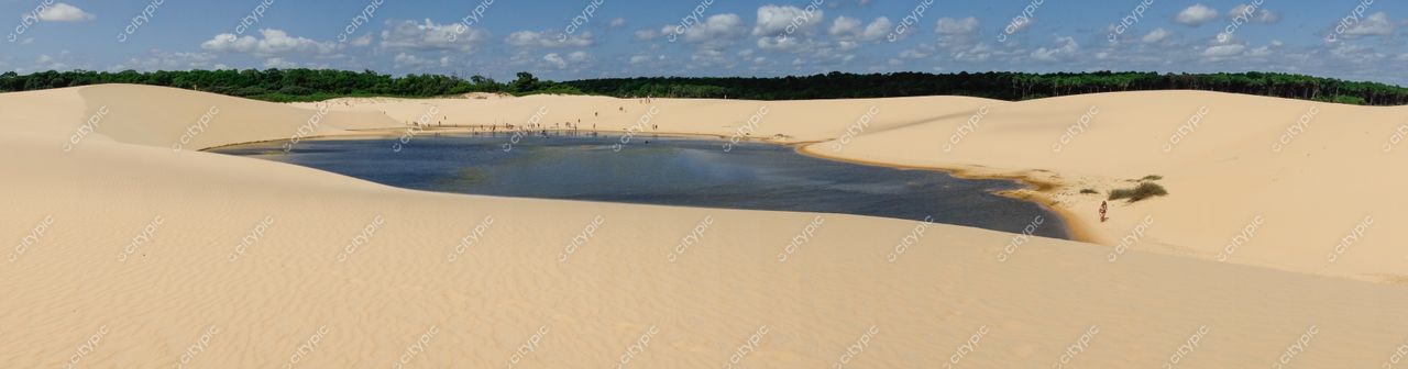 Atins, Maranhão Lagoa cercada por vegetação verde em meio a dunas de areia dourada sob céu nublado