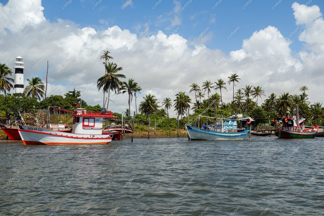Atins, Maranhão com barcos de pesca ancorados em água calma e farol listrado sob céu parcialmente nublado