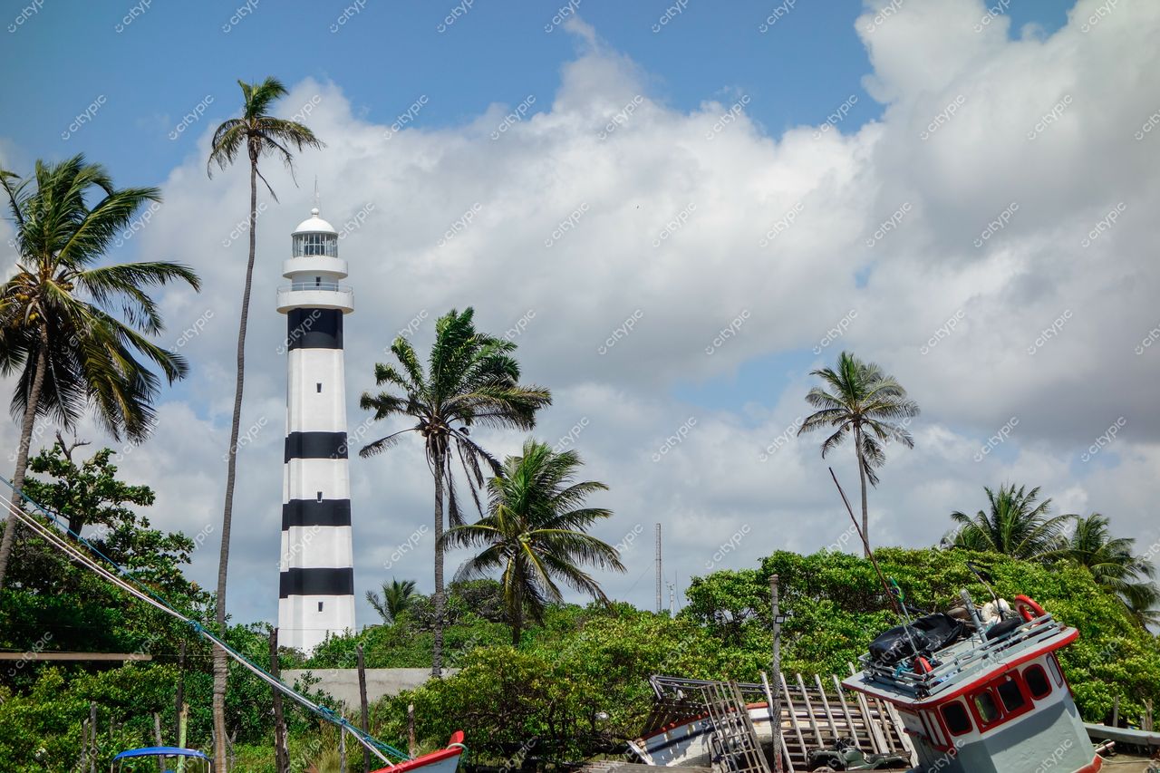 Atins, Maranhão, farol listrado em preto e branco entre palmeiras e embarcação encalhada em dia ensolarado