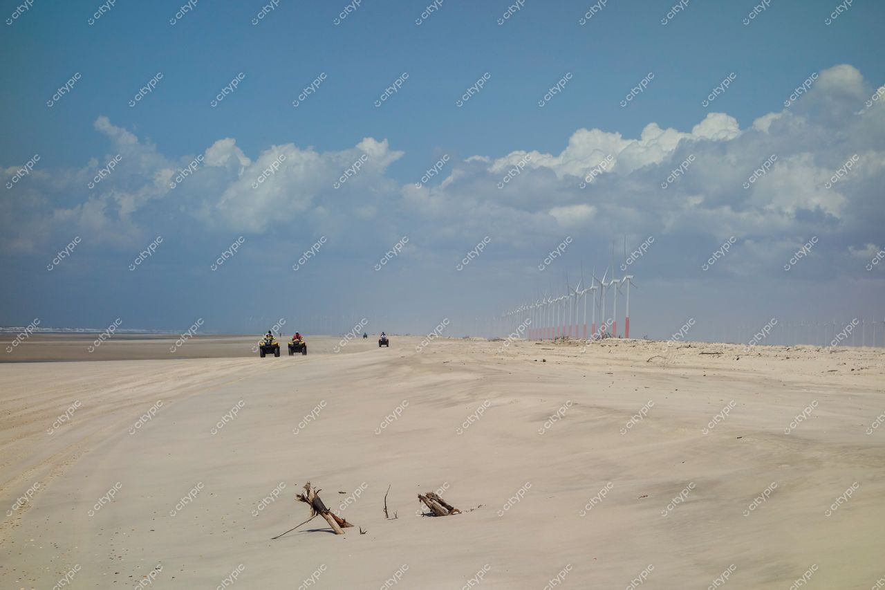 Atins, Maranhão com estrada de areia, turbinas eólicas ao fundo e quadriciclos em atividade recreativa sob céu azul