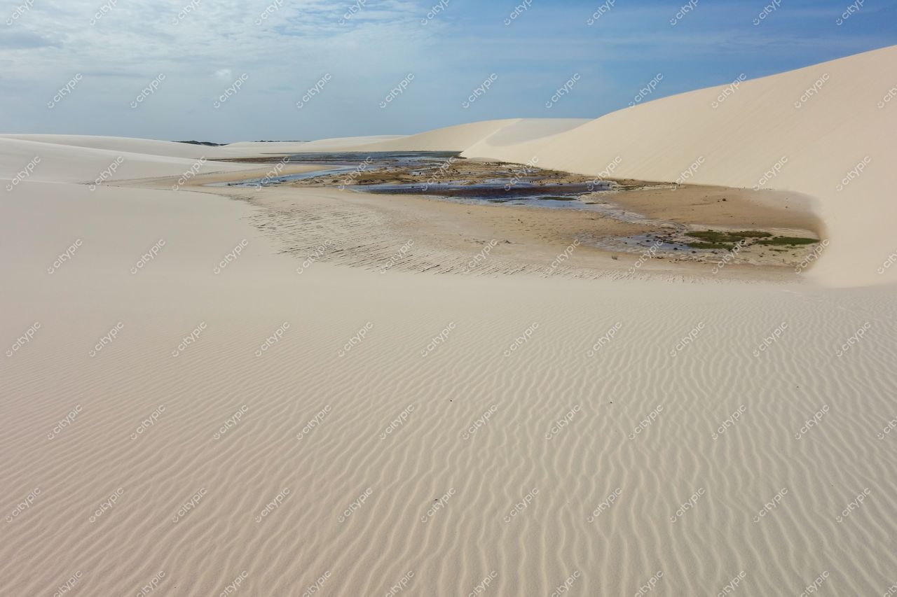Lençóis Maranhenses, Maranhão, vastas dunas de areia clara com corpo d’água refletindo luz sob céu nublado