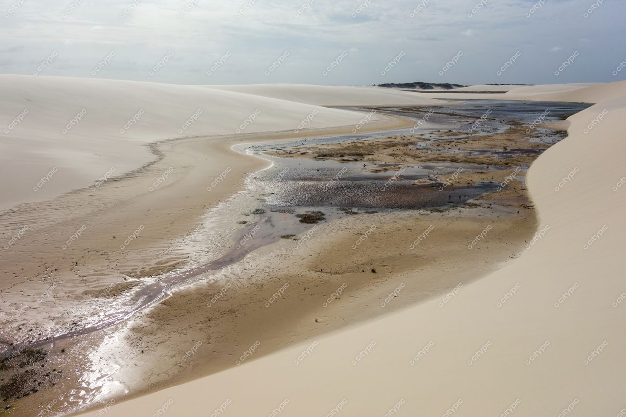 Lençóis Maranhenses, Maranhão, curso d’água tranquilo entre dunas claras em dia nublado com vegetação esparsa