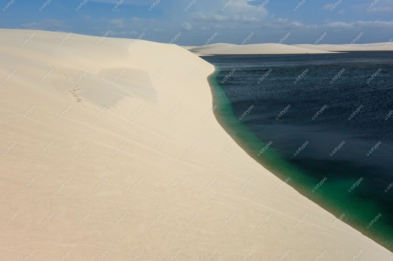 Lençóis Maranhenses, Maranhão com dunas de areia branca e lagoa azul-turquesa sob céu parcialmente nublado durante o dia