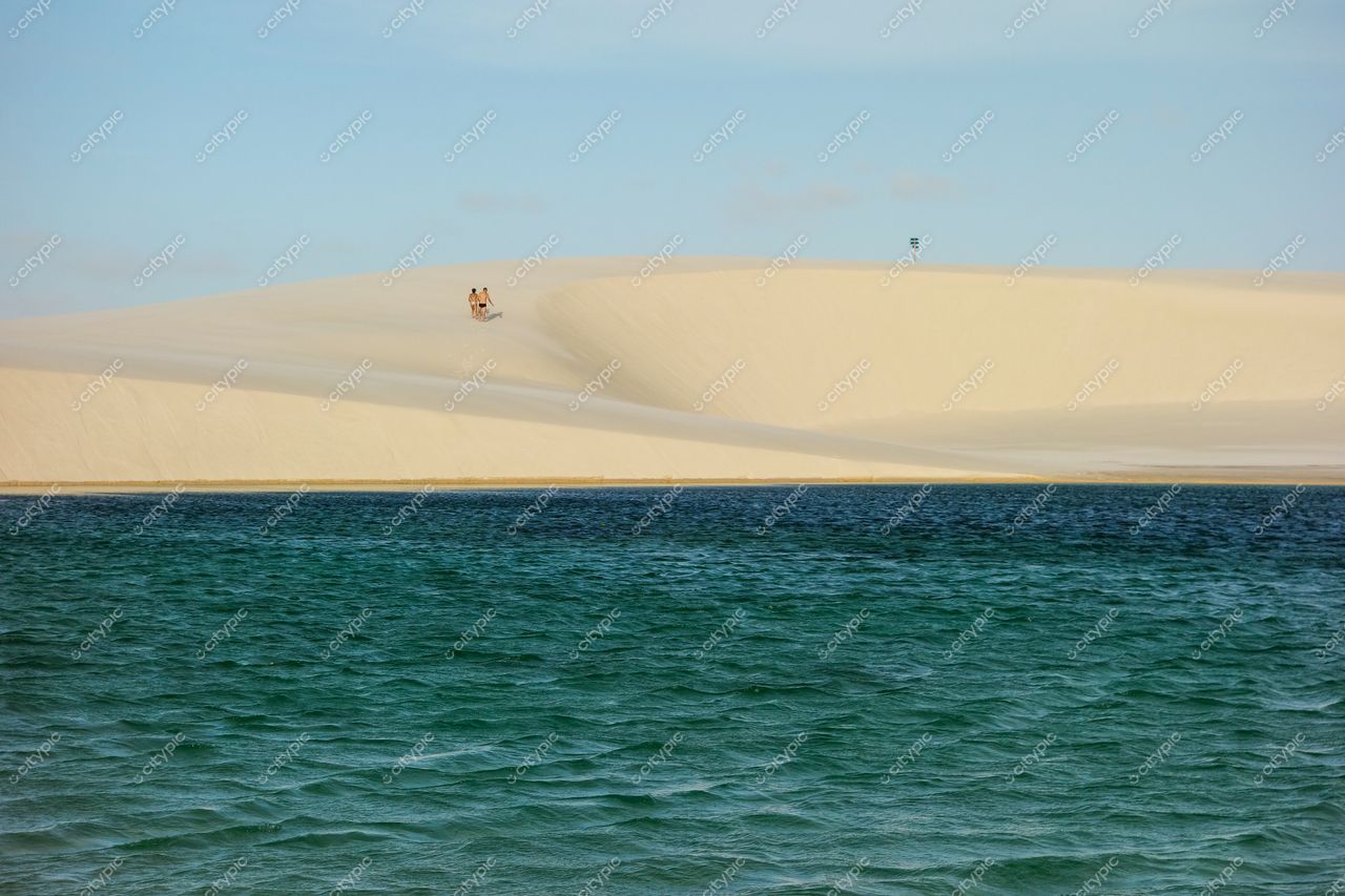Lençóis Maranhenses, Maranhão, lagoa cristalina em meio a dunas brancas com pessoas interagindo sob céu claro
