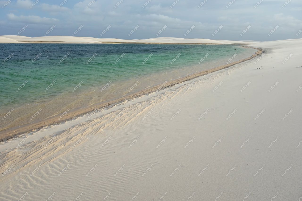 Lençóis Maranhenses, Maranhão, praia de areia branca com águas azul e verde sob céu nublado e dunas suaves ao fundo