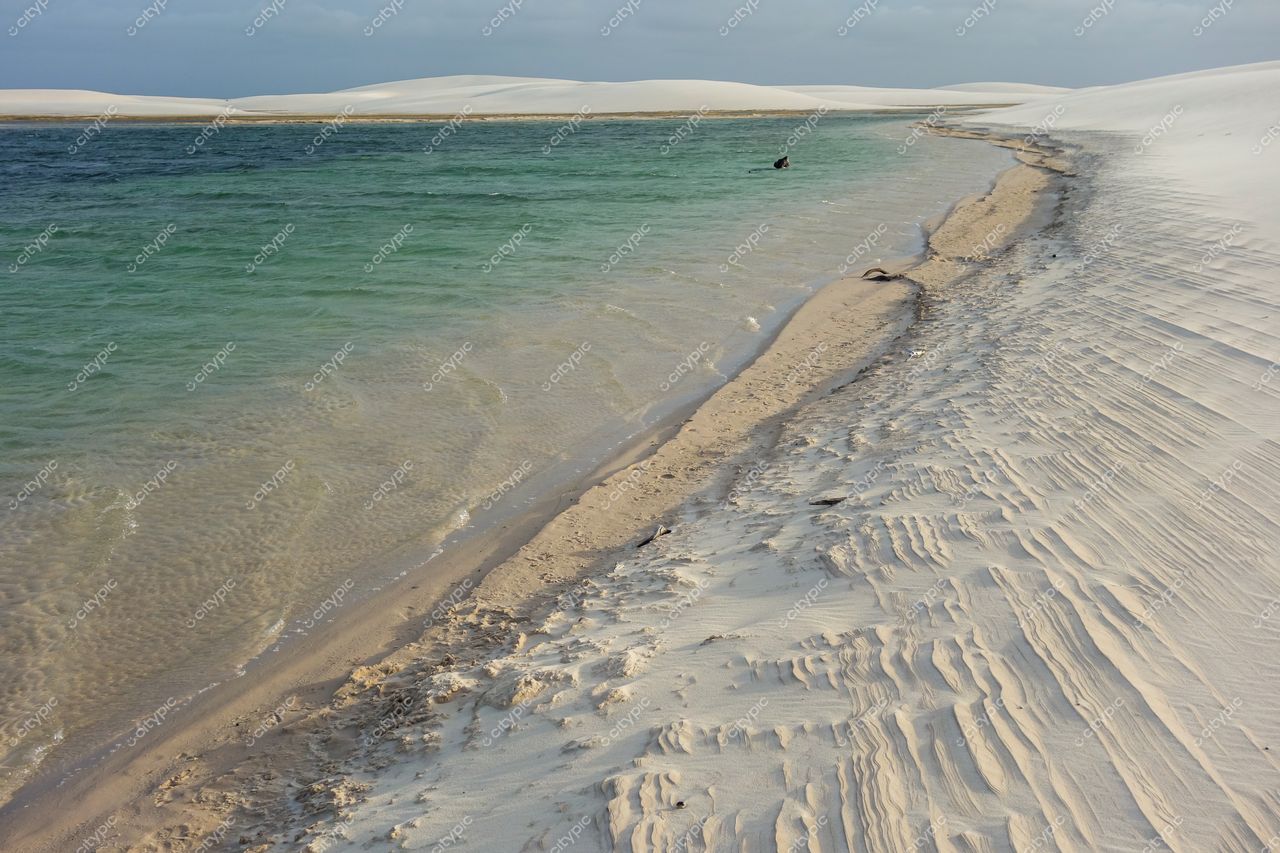 Lençóis Maranhenses, Maranhão, faixa de areia branca à direita e águas tranquilas em tons de verde e azul