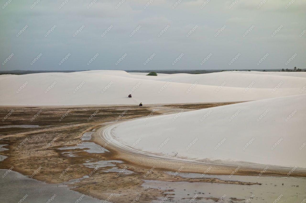 Lençóis Maranhenses, Maranhão, trilha sinuosa em meio a dunas brancas e poças d’água sob céu nublado