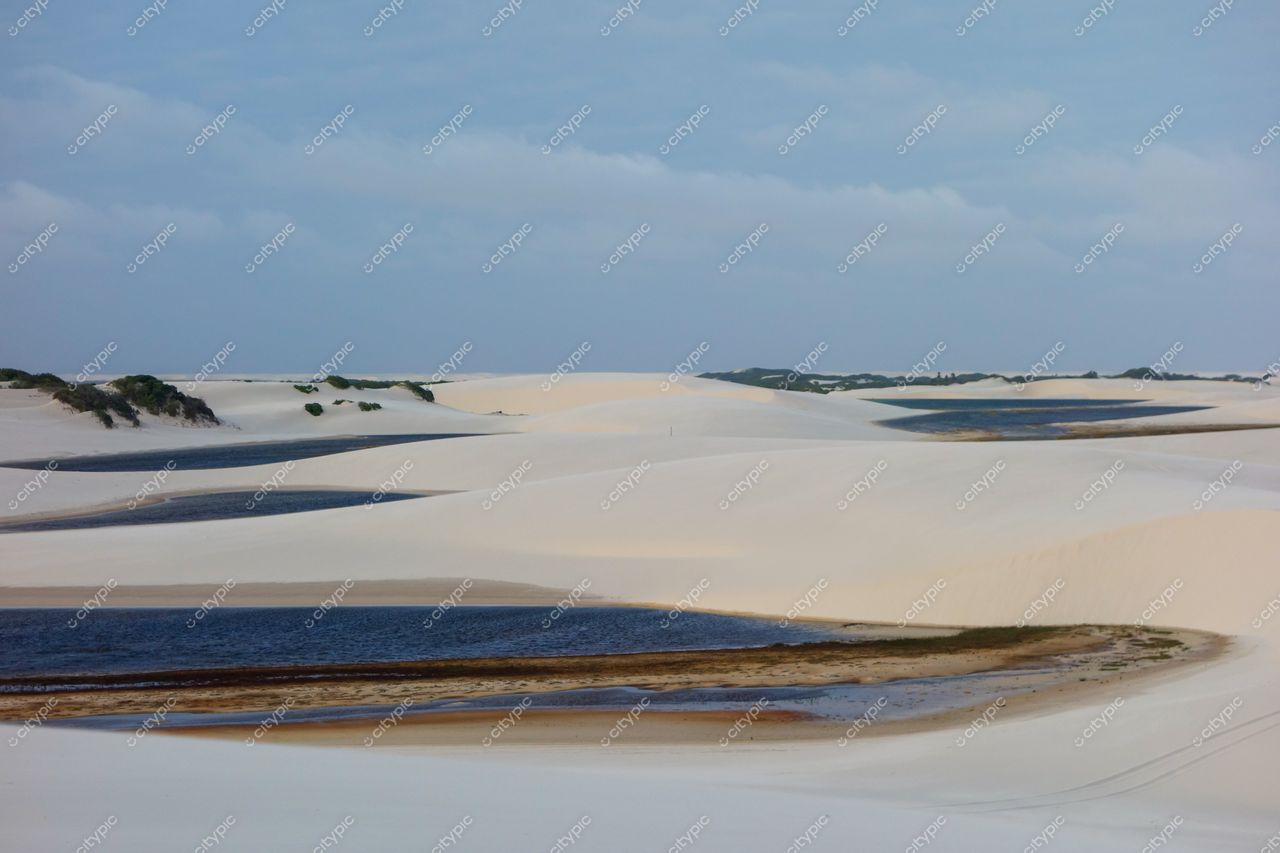 Lençóis Maranhenses, Maranhão, lagoas azuis refletindo céu nublado entre dunas brancas com vegetação rasteira ao redor