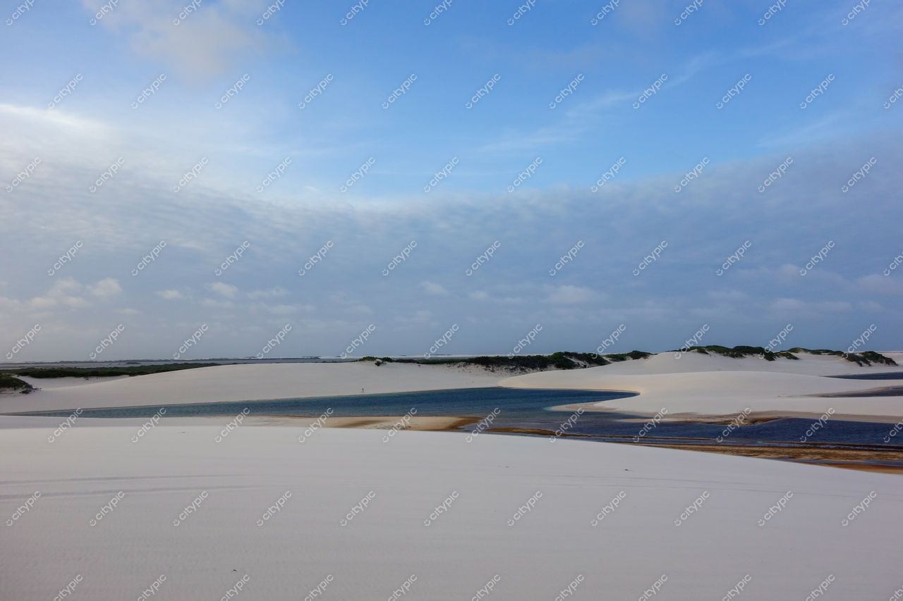 Lençóis Maranhenses, Maranhão, vastas dunas brancas e lagoas cristalinas sob céu parcialmente nublado com vegetação baixa