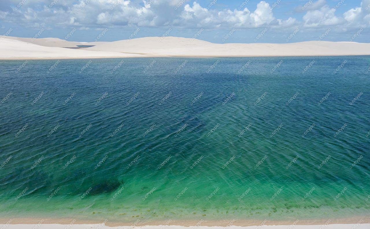 Lençóis Maranhenses, Maranhão, lago de águas cristalinas cercado por dunas brancas sob céu parcialmente nublado e iluminação suave
