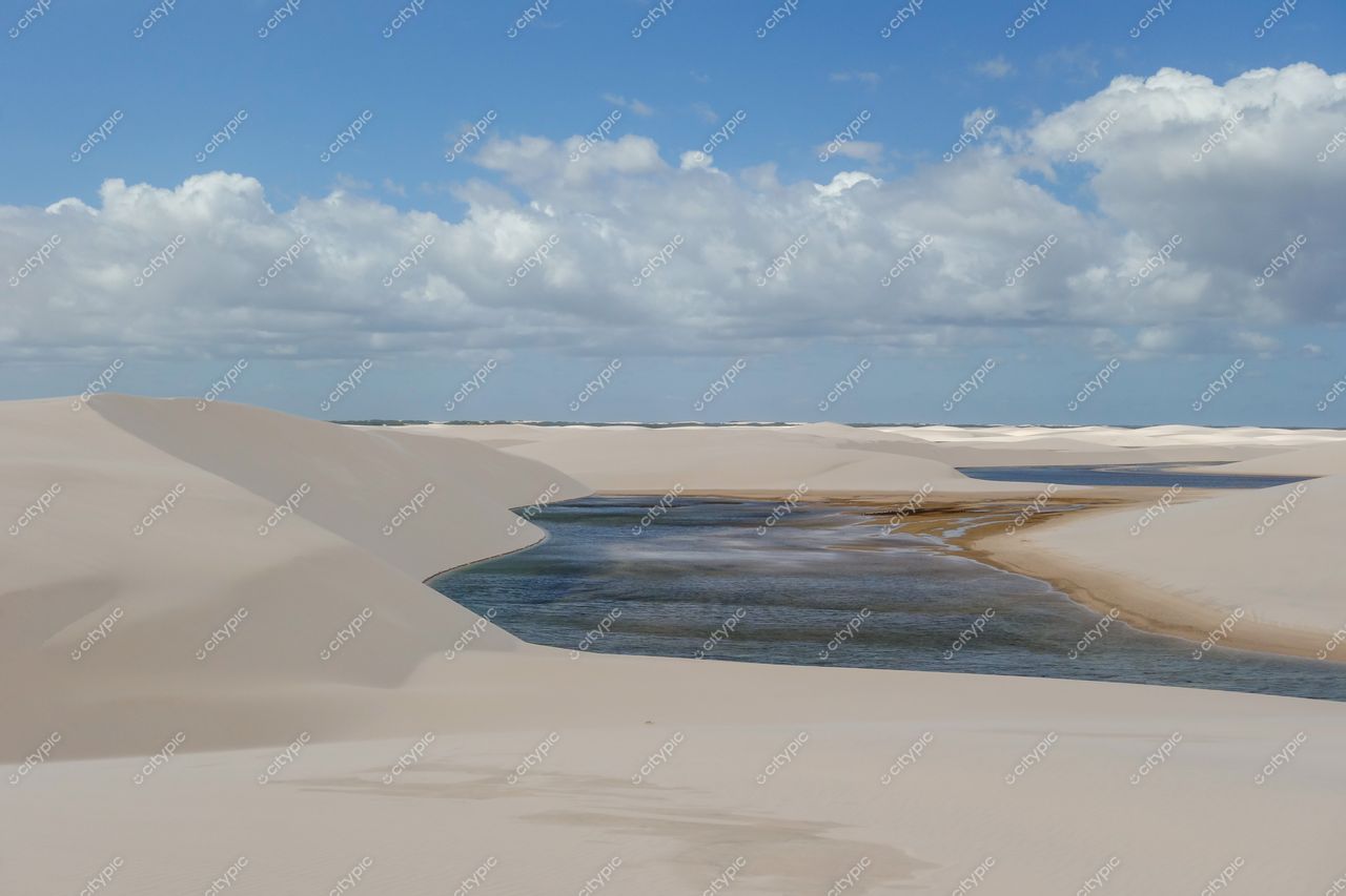 Lençóis Maranhenses, Maranhão, vastas dunas de areia clara com rio serpenteante sob céu parcialmente nublado e vegetação escassa