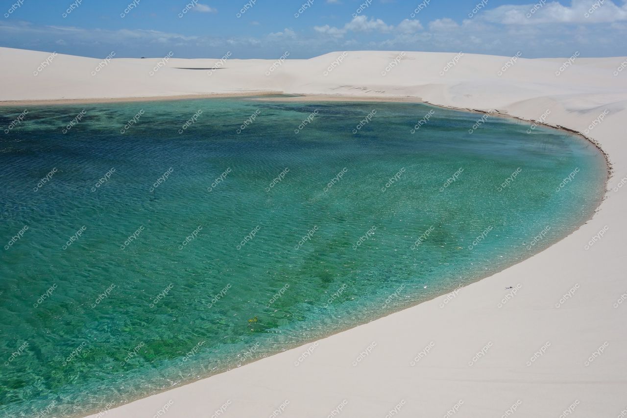 Lençóis Maranhenses, Maranhão, lagoa de águas cristalinas entre dunas brancas sob céu parcialmente nublado e relevo ondulado