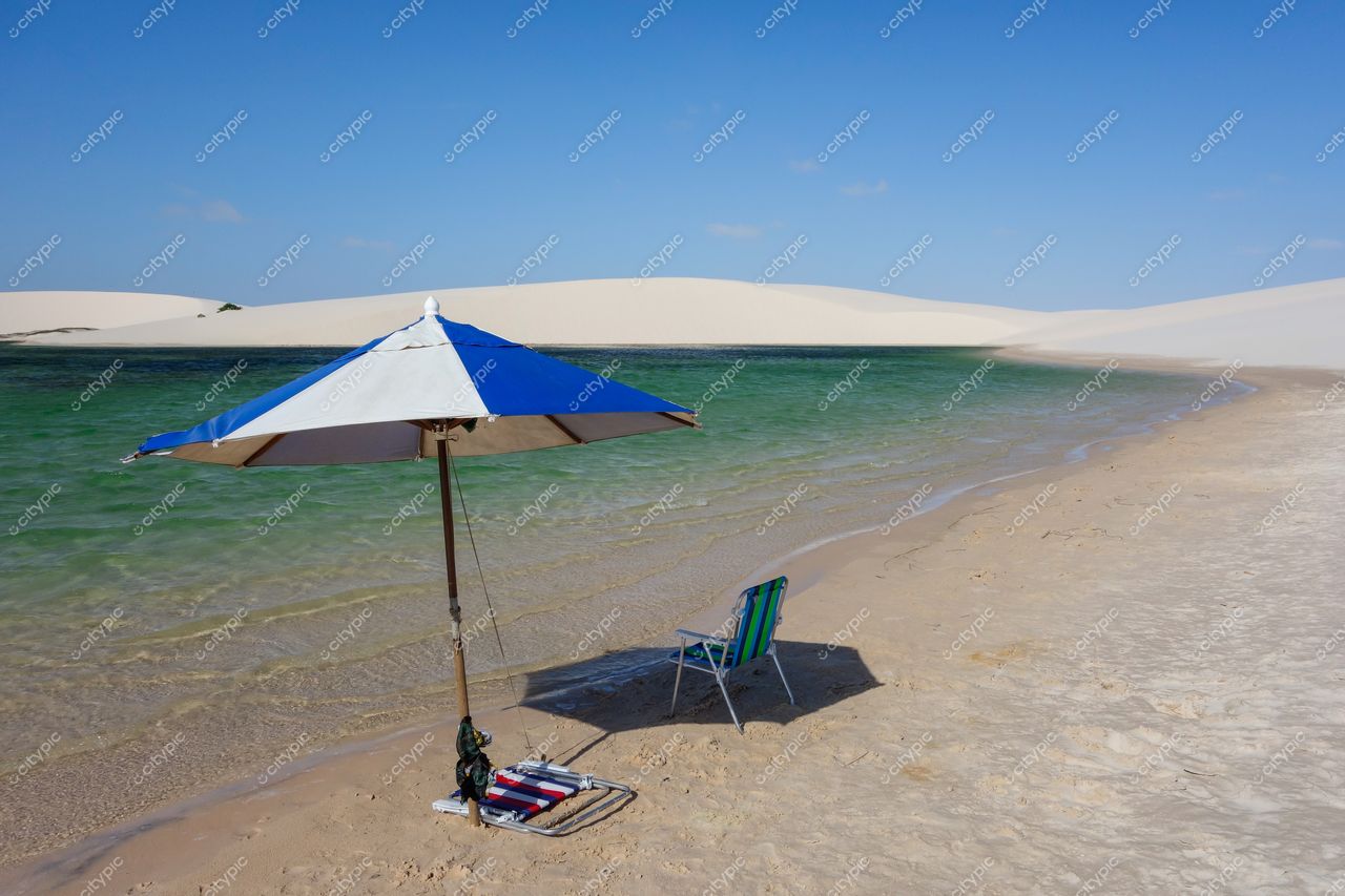 Lençóis Maranhenses, Maranhão, guarda-sol listrado azul e branco na areia clara com assento verde e águas verdes ao fundo