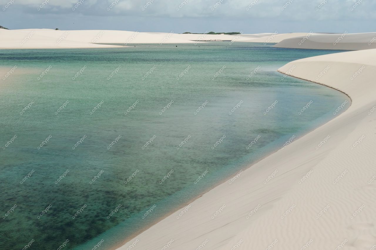 Lençóis Maranhenses, Maranhão, vista das dunas brancas e lagoa verde-azulada sob céu parcialmente nublado e iluminação suave