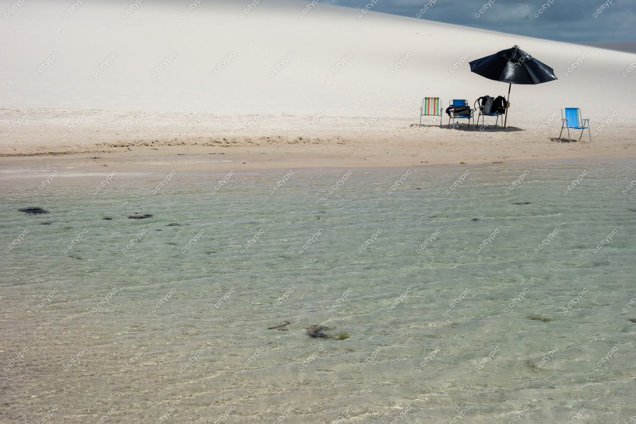 Lençóis Maranhenses, Maranhão, praia tranquila com cadeiras e guarda-sol preto em areia clara sob céu nublado