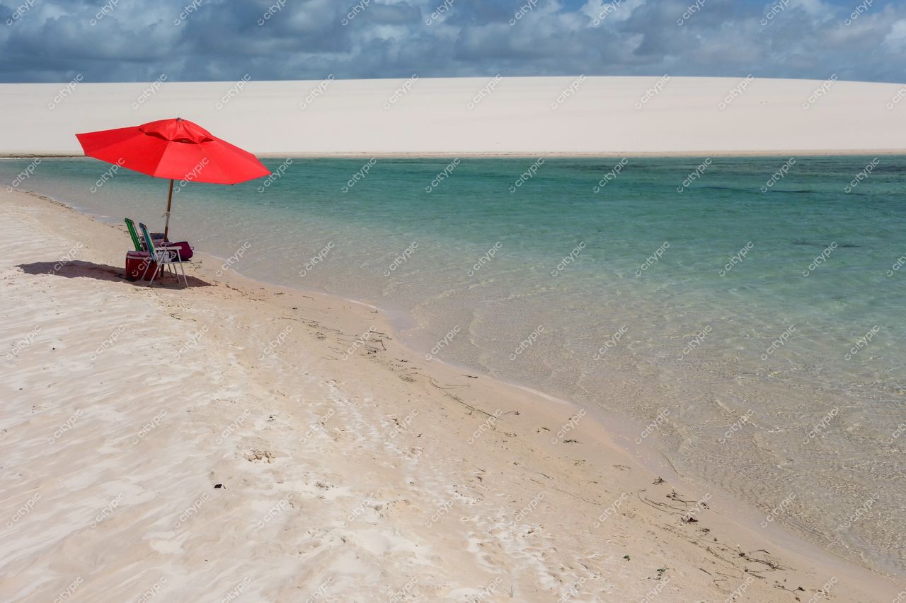 Lençóis Maranhenses, Maranhão, lago de águas cristalinas com cadeira e guarda-sol vermelho em dia ensolarado