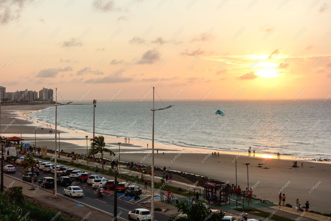 São Luís, Maranhão, pôr do sol na praia com reflexos coloridos e pessoas caminhando na areia e calçada