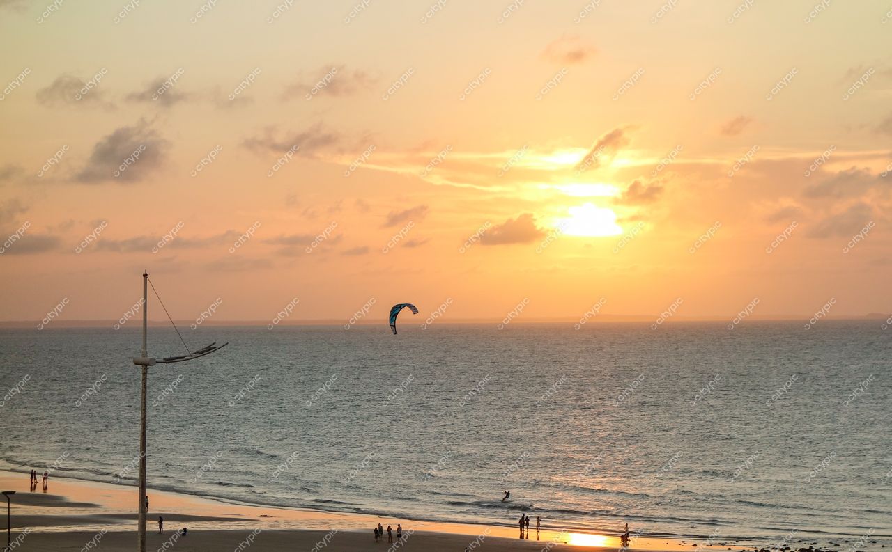 São Luís, Maranhão, pôr do sol na praia com kitesurfista ao fundo e pessoas caminhando na areia