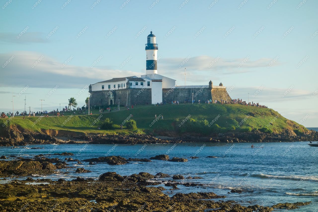 Salvador, Bahia, Farol da Barra em dia ensolarado com mar sereno e pessoas no gramado ao redor