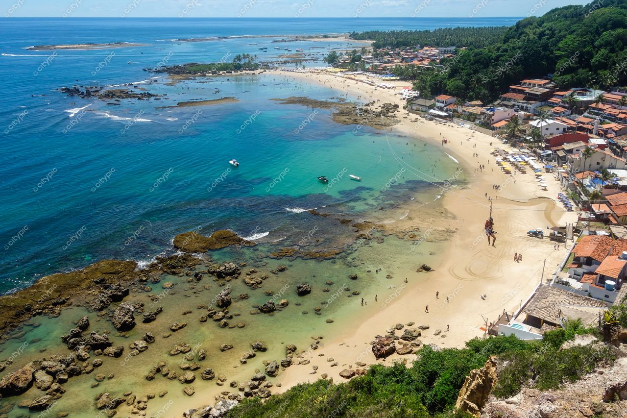 Morro de São Paulo, Bahia vista aérea com praia clara, espreguiçadeiras brancas e casas coloridas em colina verdejante