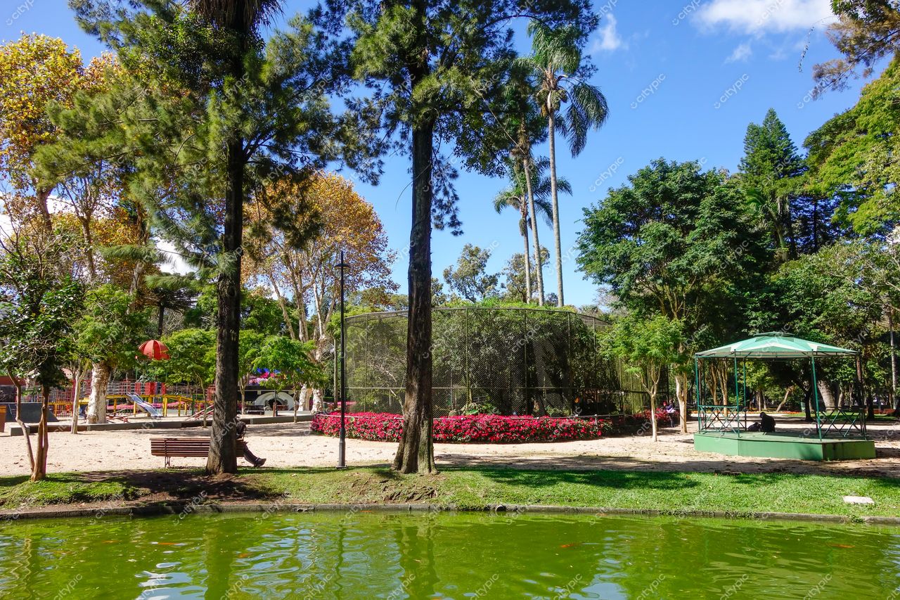 Curitiba, Paraná, parque arborizado com lago verde, gazebo de metal e canteiros floridos em dia claro